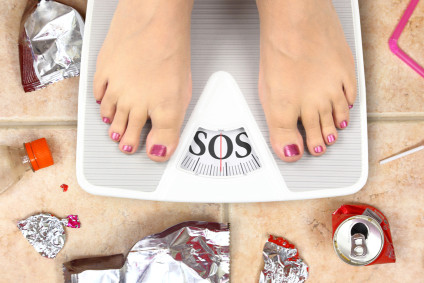 Feet on bathroom scale with word SOS and junk food garbage